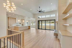 Living room with sink, ceiling fan with notable chandelier, a high ceiling, and light wood-type flooring