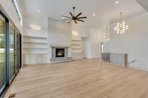 Unfurnished living room featuring light wood-type flooring, a towering ceiling, built in features, and ceiling fan with notable chandelier