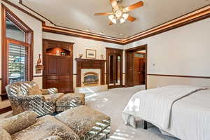 Bedroom with ceiling fan, crown molding, carpet, and a tile fireplace