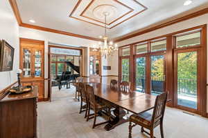 Carpeted dining space with a wealth of natural light, crown molding, and an inviting chandelier