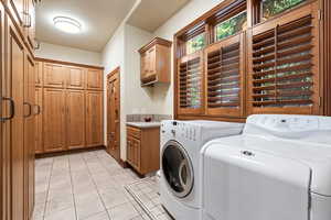 Laundry room with washer and dryer, light tile patterned flooring, and cabinets