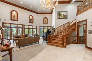 Living room featuring light tile patterned floors, an inviting chandelier, ornamental molding, a high ceiling, and french doors