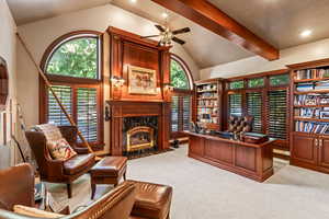 Carpeted office with a premium fireplace, vaulted ceiling with beams, and ceiling fan