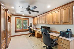 Office space with built in desk, crown molding, light colored carpet, a textured ceiling, and ceiling fan