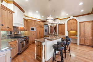 Kitchen featuring backsplash, a kitchen island with sink, stone countertops, built in appliances, and light hardwood / wood-style floors