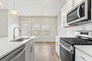 Kitchen with sink, stainless steel appliances, light hardwood / wood-style floors, decorative backsplash, and white cabinets