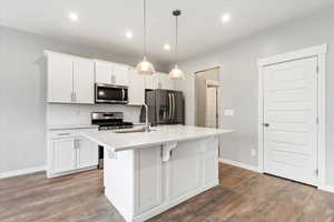 Kitchen with a center island with sink, sink, appliances with stainless steel finishes, white cabinetry, and wood-type flooring