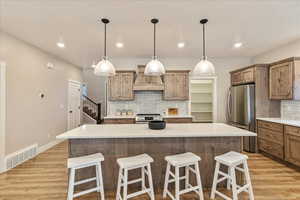 Kitchen featuring appliances with stainless steel finishes, light wood-type flooring, backsplash, custom exhaust hood, and a large island