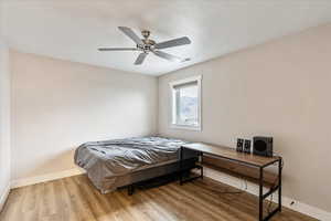 Bedroom with ceiling fan, light wood-type flooring, and a textured ceiling