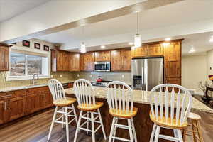 Kitchen with a breakfast bar, decorative backsplash, dark hardwood / wood-style flooring, and stainless steel appliances