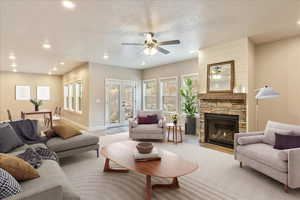 Living room featuring french doors, light wood-type flooring, a textured ceiling, ceiling fan, and a fireplace