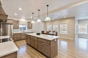 Kitchen with a center island, stainless steel fridge, decorative light fixtures, decorative backsplash, and light wood-type flooring