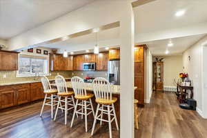 Kitchen with backsplash, a kitchen breakfast bar, hanging light fixtures, dark hardwood / wood-style floors, and stainless steel appliances