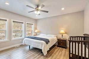 Bedroom featuring a textured ceiling, light wood-type flooring, multiple windows, and ceiling fan