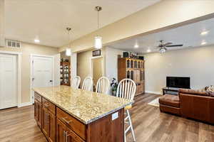 Kitchen with a kitchen breakfast bar, ceiling fan, wood-type flooring, a kitchen island, and hanging light fixtures