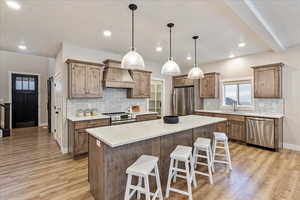 Kitchen with light hardwood / wood-style floors, a kitchen island, premium range hood, and stainless steel appliances