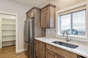 Kitchen with light wood-type flooring, sink, stainless steel refrigerator, and tasteful backsplash