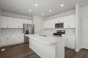 Kitchen featuring an island with sink, stainless steel appliances, white cabinetry, and sink