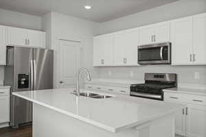 Kitchen featuring stainless steel appliances, white cabinetry, a kitchen island with sink, and sink