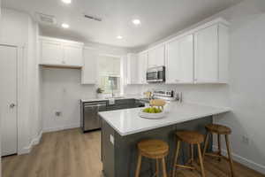 *Model Home Photo. Kitchen featuring white cabinets, sink, light hardwood / wood-style flooring, appliances with stainless steel finishes, and kitchen peninsula