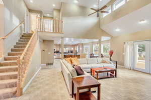 Living room featuring ceiling fan, light carpet, and a high ceiling