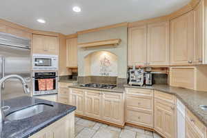 Kitchen with dark stone counters, sink, built in appliances, light brown cabinetry, and light tile patterned flooring