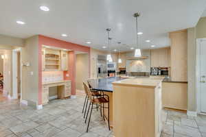 Kitchen with backsplash, built in appliances, pendant lighting, light brown cabinetry, and a kitchen island