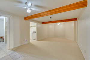 Carpeted empty room with beamed ceiling, washer / dryer, and ceiling fan