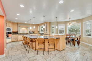 Kitchen featuring light brown cabinets, stainless steel oven, white microwave, a kitchen breakfast bar, and kitchen peninsula