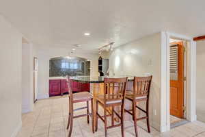 Kitchen featuring tasteful backsplash, kitchen peninsula, track lighting, a textured ceiling, and light tile patterned flooring