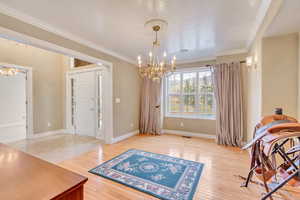 Interior space featuring an inviting chandelier, crown molding, and light hardwood / wood-style flooring