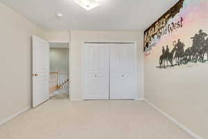 Unfurnished bedroom featuring a textured ceiling, light colored carpet, and a closet