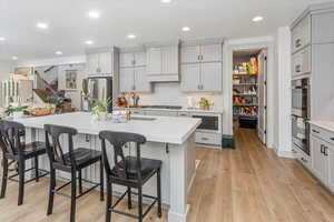 Kitchen with stainless steel appliances, a kitchen breakfast bar, gray cabinets, a center island with sink, and light wood-type flooring