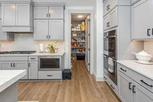 Kitchen featuring appliances with stainless steel finishes, premium range hood, light stone counters, light hardwood / wood-style floors, and gray cabinets