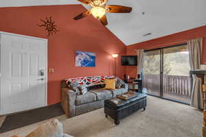 Carpeted living room with ceiling fan and vaulted ceiling