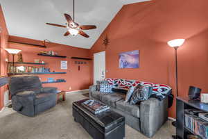 Carpeted living room featuring ceiling fan and high vaulted ceiling