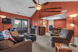 Carpeted living room featuring a skylight, ceiling fan, a stone fireplace, and high vaulted ceiling