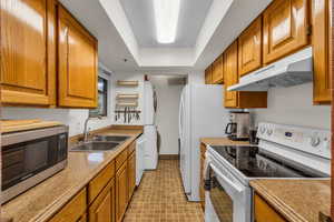 Kitchen featuring white appliances, sink, and a tray ceiling