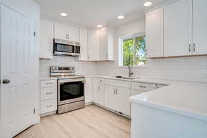 Kitchen with sink, white cabinets, light wood-type flooring, and appliances with stainless steel finishes