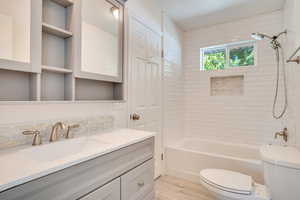 Full bathroom with hardwood / wood-style flooring, toilet, decorative backsplash, vanity, and tiled shower / bath