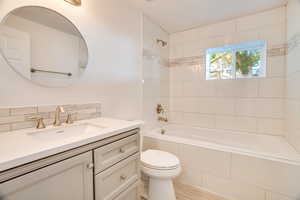 Full bathroom with tasteful backsplash, vanity, tiled shower / bath combo, hardwood / wood-style flooring, and toilet