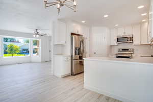 Kitchen with kitchen peninsula, white cabinetry, stainless steel appliances, and light hardwood / wood-style flooring