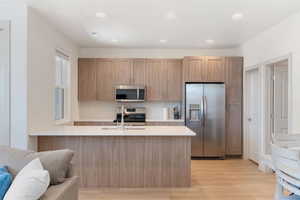 Kitchen with light brown cabinetry, light hardwood / wood-style flooring, stainless steel appliances, and sink