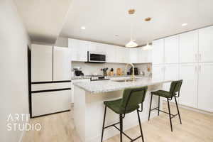 Kitchen featuring white cabinetry, sink, an island with sink, light hardwood / wood-style floors, and white appliances