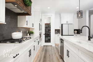 Kitchen with stainless steel appliances, light stone counters, white cabinets, exhaust hood, and light wood-type flooring