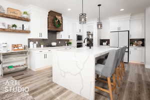 Kitchen with a center island with sink, decorative backsplash, white cabinetry, and light hardwood / wood-style flooring