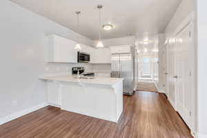 Kitchen featuring kitchen peninsula, pendant lighting, stainless steel appliances, and white cabinets