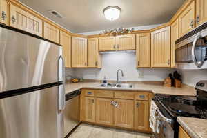 Kitchen featuring sink, light tile patterned flooring, a textured ceiling, and appliances with stainless steel finishes