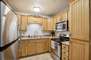 Kitchen featuring appliances with stainless steel finishes, a textured ceiling, light tile patterned floors, and sink