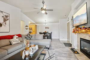 Living room featuring a fireplace, ceiling fan with notable chandelier, light hardwood / wood-style flooring, and lofted ceiling